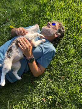 Man Lying On Grass Playing With Blue Merle Border Collie Puppy