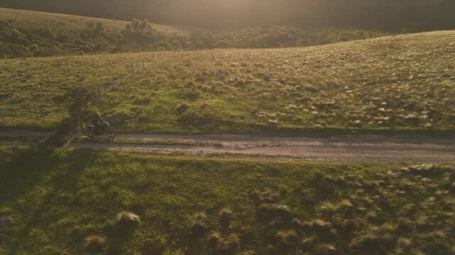 Vista a&eacute;rea de uma mulher pilotando uma motocicleta em uma estrada de terra deserta no alto da montanha no nascer do sol