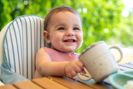 Smiling Baby Holding Cup Outdoors In High Chair