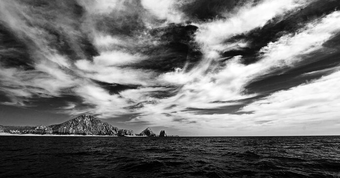 Lands End under dramatic cloudscape as seen from the Pacific Ocean at Cabo San Lucas in Baja California Mexico BCS - black and white