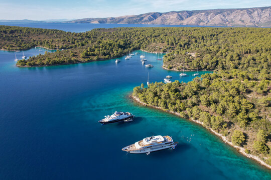 Aerial view of yachts resting in the turquoise Jack Sparrow Bay surrounded by vibrant green forests near Stari Grad, Hvar island, Dalmatian Coast, Croatia.