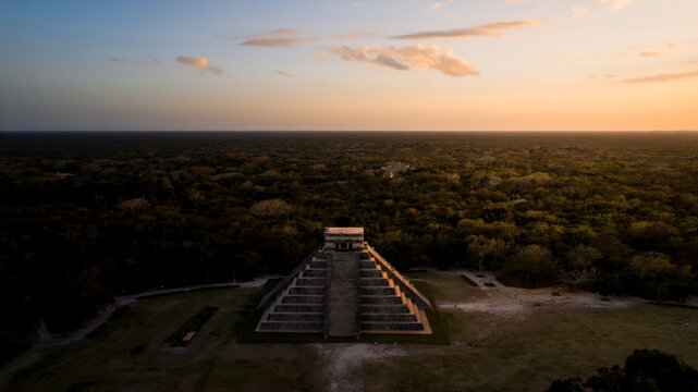 Aerial view of the ancient Mayan step pyramid El Castillo stands majestically amidst a sea of green jungle, under a warm, golden sunset sky, Chichen-Itza, Yucatan, Mexico.