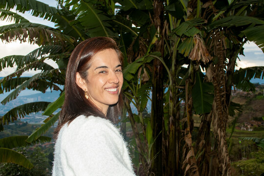 Smiling Woman Poses Near Lush Banana Trees in Scenic Landscape