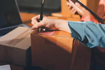 Obraz premium Startup SME small business entrepreneur of freelance Asian woman wearing apron using laptop and box to receive and review orders online to prepare to pack sell to customers, online sme business ideas.