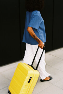 Traveler woman walking with yellow suitcase on street, film photo