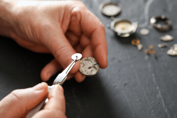 Senior man fixing mechanism of vintage wrist watch at black table, closeup. Space for text