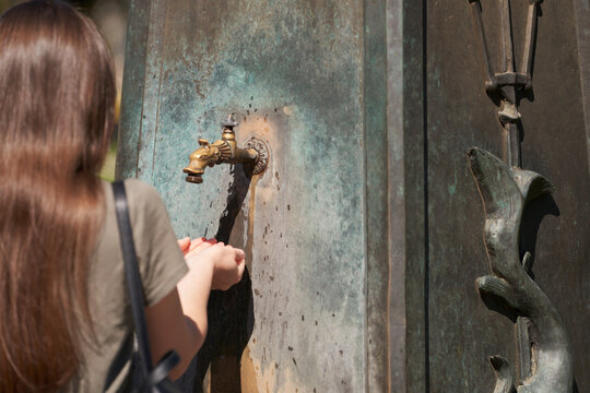 A young woman scoops water from a drinking fountain into her palms. Close-up.
