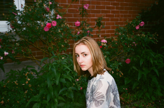 Young Woman in Floral Shirt Sitting by Garden Roses