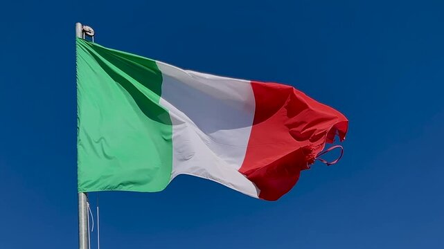 Italian tricolor flag waving in the wind on pole against a clear blue sky