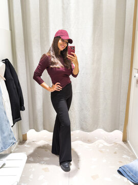 Woman taking mirror selfie while trying on clothes in fitting room
