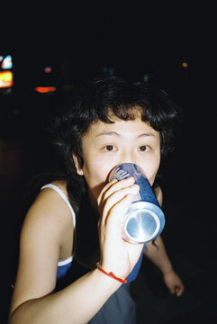 Asian woman drinking from a can 