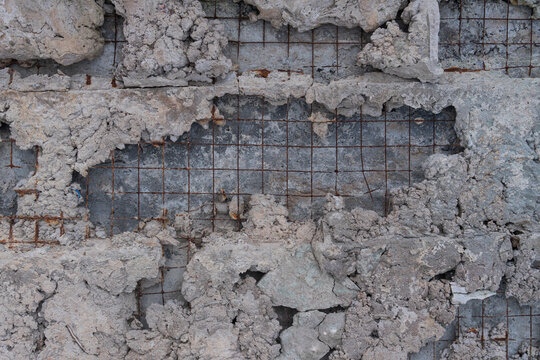 Gritty, detailed background of a decaying gray concrete surface. Crumbling plaster reveals a rusty metal rebar grid, creating an industrial, abstract, and worn texture. Flat lay composition.