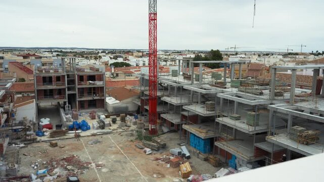 High-angle view sprawling construction site of new housing development, detailing concrete frames and brickwork of multi-story buildings surrounding central courtyard.Real estate development concept.
