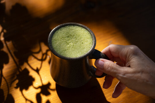 Drinking matcha latte drink on sunlit table 