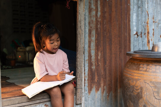 Thai rural child reading a book by a zinc house window