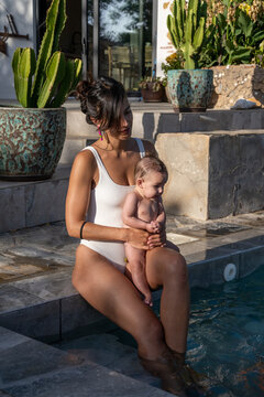 Woman Holding Baby While Sitting At Pool Edge