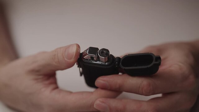 Male hands opening electronic flameless lighter, activating plasma arc with modern usb rechargeable device featuring flexible neck for lighting candles. Shooting in slow motion.