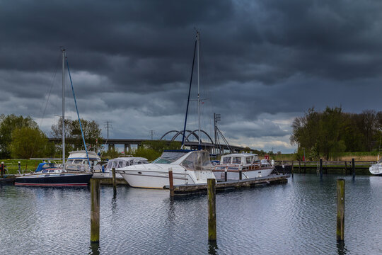 Stormy sky above a quiet marina with sailboats and reflections on the shore. In the background, a highway bridge over the St&ouml;r River. Itzehoe. Germany.
