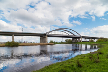 Obraz premium Highway bridge spanning the Stör River near Itzehoe, Schleswig-Holstein, Germany, under blue sky and spring landscape.