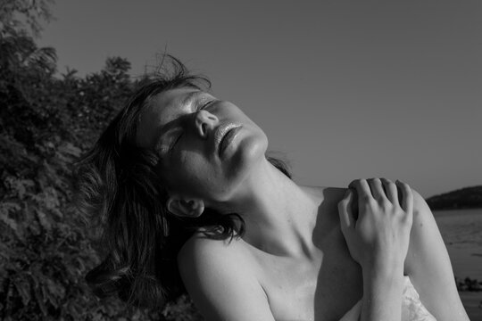 A naked woman sits on a stone by the river.