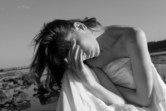 A naked woman sits on a stone by the river.