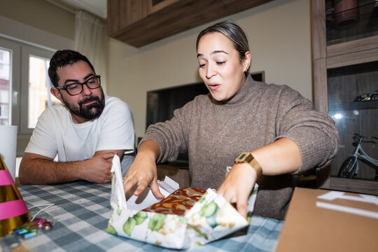 Woman unwrapping gift from man during birthday celebration