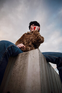 Young Person Sitting on Concrete Block While Talking on Phone