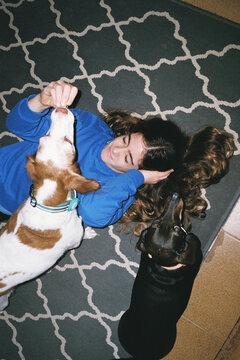 Girl Lying on Floor Feeding Two Dogs
