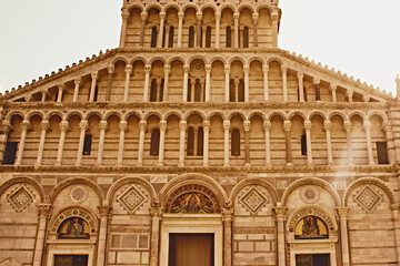 Obraz premium Historic facade of Pisa Cathedral illuminated by warm golden evening light in Pisa, Italy. Iconic European travel destination featuring Romanesque architecture, marble details and symmetrical arches. 