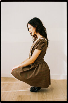 Side profile of woman in brown dress kneeling indoors