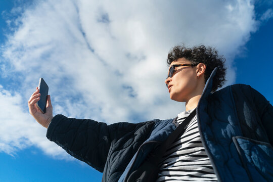 Woman using phone against blue sky with white clouds