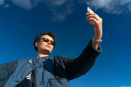 Casual woman taking selfie against blue sky with white clouds