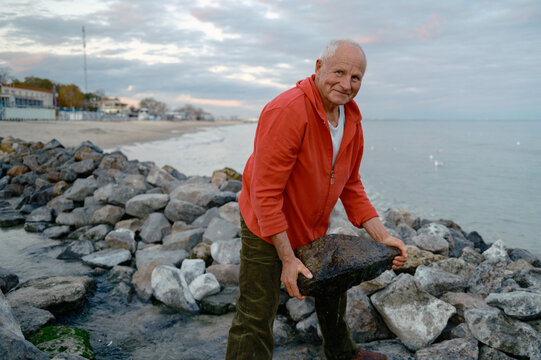 An elderly man is beautifying a part of the beach by the sea.