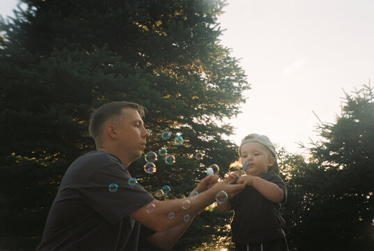 Father and toddler playing with soap bubbles at sunset, film photo
