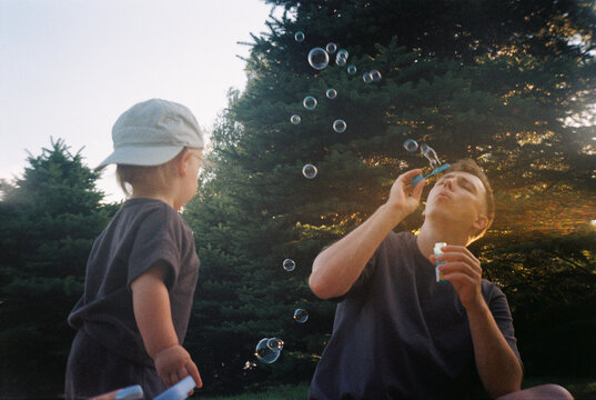 Father blowing soap bubbles for toddler outdoors  - film analog