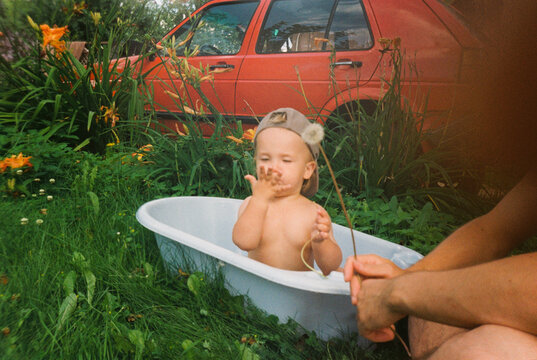 Toddler in tub outdoors playing with dandelion in summer - film analog