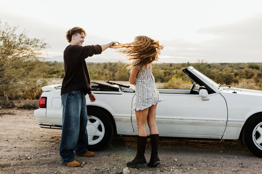 Young couple dancing in front of convertible 