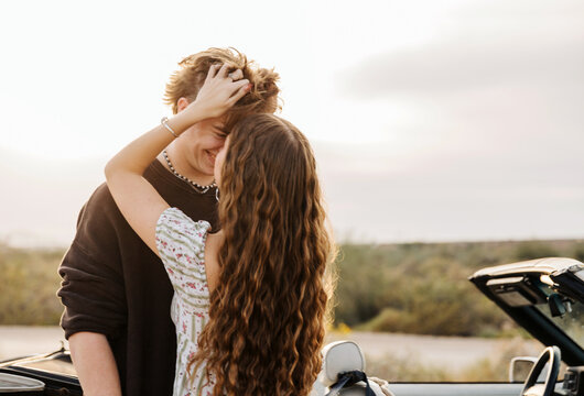 Girlfriend tossing boyfriend's hair in front of convertible 