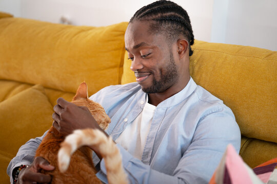 Man cuddling ginger cat on sofa at home