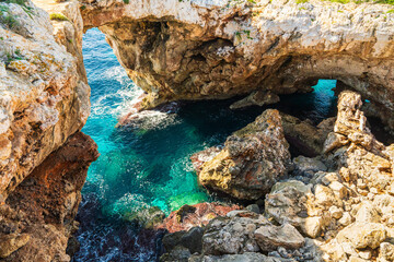 Naklejka premium Pont Natural dEs Calo Blanc, natural stone arch above clear turquoise water in Mallorca. Dramatic coastal landscape and Mediterranean nature.
