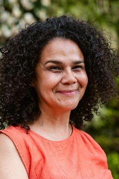 Smiling Woman With Curly Hair Wearing Orange in Natural Setting