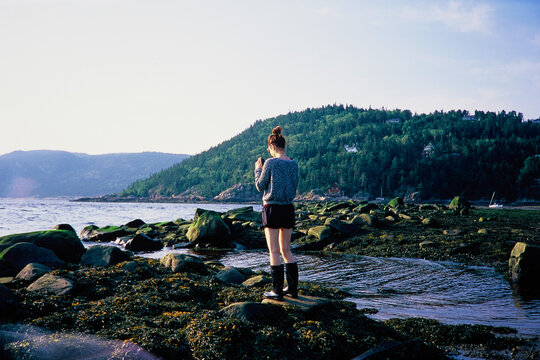 Woman Walking Along Mossy Shoreline at Sunset