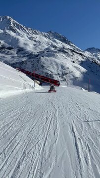 A natural sledding and ski slope on a sunny winter day with a red Swiss train view in Andermatt, Switzerland. Wonderful mountain landscape with fresh alpine snow cover of the Swiss Alps