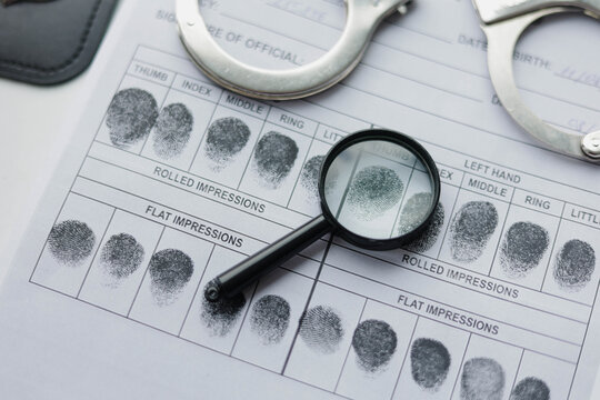 Forensic identification concept with fingerprint cards, handcuffs and magnifying glass. Crime investigation, biometric identification and law enforcement tools.