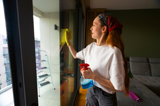 Woman cleaning apartment window using spray and cloth
