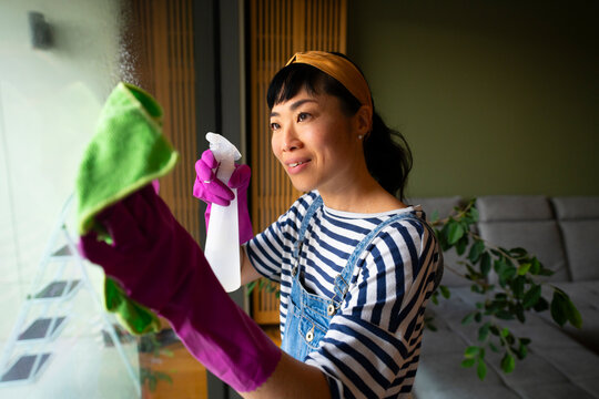 Young woman cleaning window with spray bottle