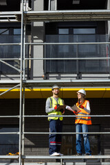 Fototapeta premium Male and female engineers reviewing project blueprints, digital tablet, and construction logbook on site.