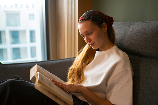 Woman relaxing at home, reading a book on sofa
