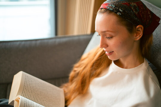 Redhead woman relaxing on sofa reading book
