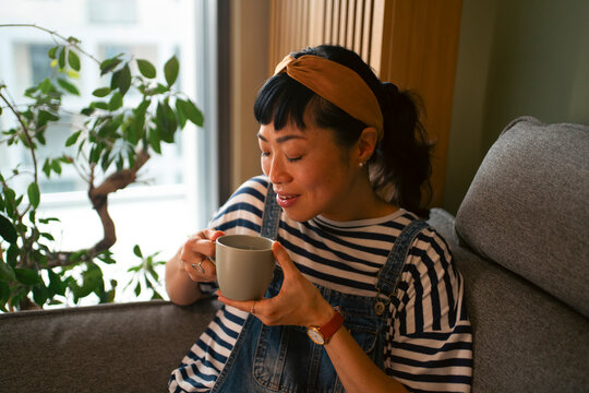 Woman enjoying hot drink sitting on sofa at home
